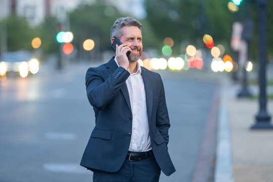 Business talk. Businessman talking on smartphone while walking in the city at night. Business late call. Business conversation overtime work. Business man man in a suit speaking on the phone outdoor.