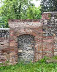 A weathered wall combines stone and brick materials, featuring an arched niche. Lush greenery surrounds the structure, highlighting its historical charm