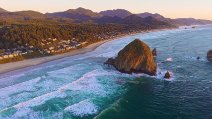 A stunning high-angle video capturing the iconic Haystack Rock and Cannon Beach shoreline bathed in the warm, golden, and vibrant hues of a sunset over the Pacific Ocean - Powered by Adobe