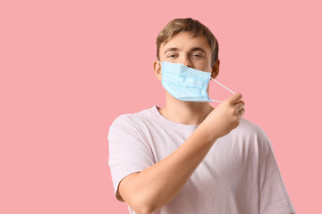 Happy young man wearing medical mask on pink background