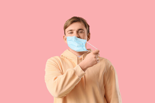 Happy young man wearing medical mask on pink background
