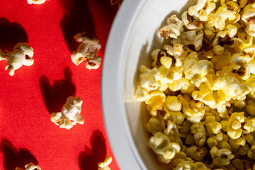 Tasty popcorn on red background, flat lay. Space for text, with a remote on the side, entertainment snacks