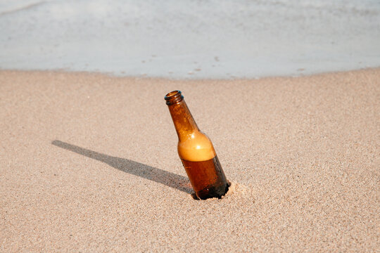 wide shot of a foamy beer bottle buried in sand at the beach