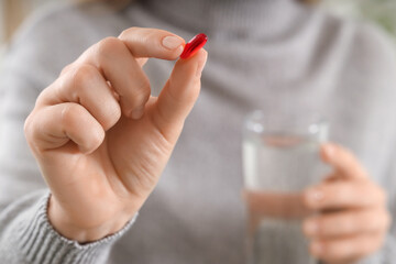 Woman with vitamin E pill and glass of water at home, closeup