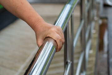 Close-up of Senior Woman's Hands Holding a Stainless Steel Handrail or Handrail for Safety on Walk Way.