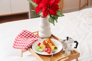 Breakfast with pancakes and Christmas plant poinsettia on bed in room