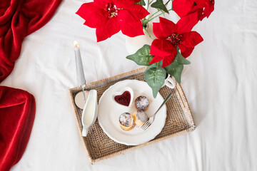 Tray with cottage cheese pancakes and Christmas plant poinsettia on bed, top view