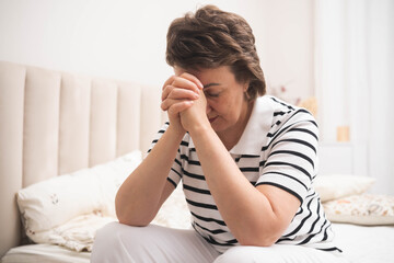 Depressed mature woman sitting in bedroom