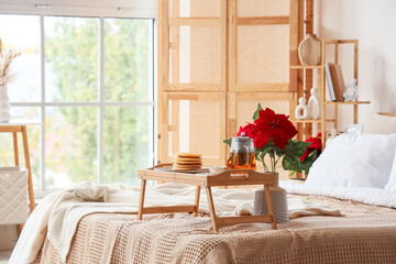 Tasty breakfast with pancakes and Christmas plant poinsettia on bed in room
