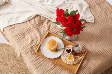 Tasty breakfast with pancakes and Christmas plant poinsettia on bed, top view