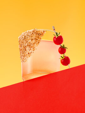 Tomato cocktail against yellow background with fresh tomato garnish