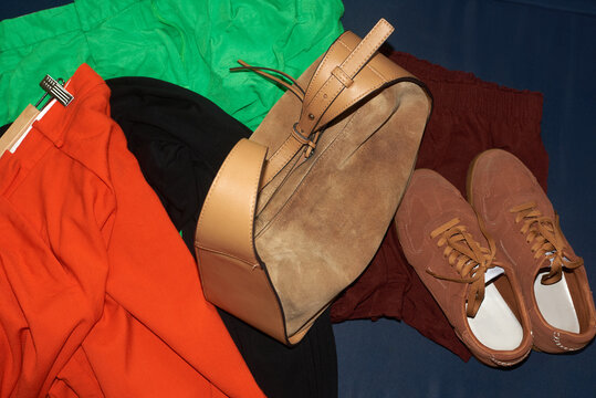 Stylish brown handbag and shoes atop a colorful array of clothing
