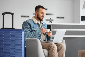 Young man with coffee and laptop waiting for his flight in airport lounge