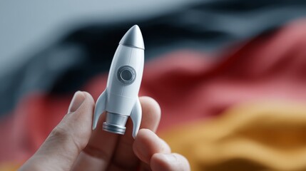 A hand holding a miniature rocket against a blurred German flag background, symbolizing innovation and ambition.