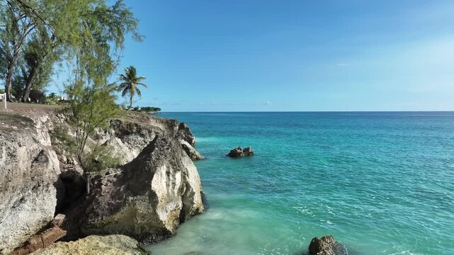 Turquoise waves washing rocky cliffs under clear skies along the Barbados coastline