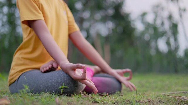 Close up shot of a woman sitting in lotus position on grass field in early morning, symbolizing peace, mindfulness, and spiritual focus in nature.