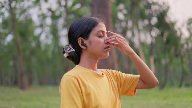 Serene woman performing alternate nostril breathing exercise with wireless earphones at outdoor during golden hour.