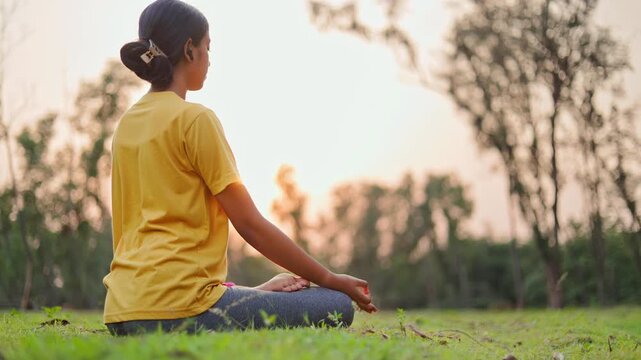 Serene woman sitting in padmasana pose in the grass field at sunrise.