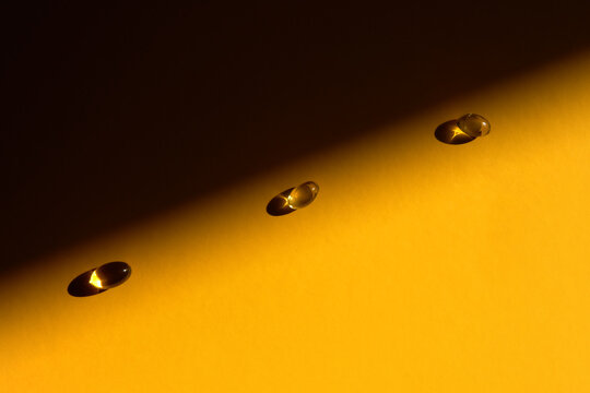 Three Golden Omega 3 Capsules on Orange Backdrop with Copy Space