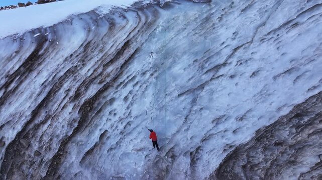 Alpinist climbing a sheer frozen waterfall on a massive glacier
