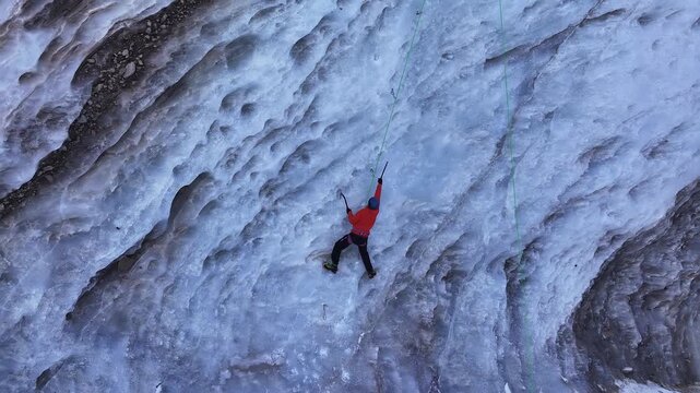 Aerial view of a man climbing a massive frozen waterfall