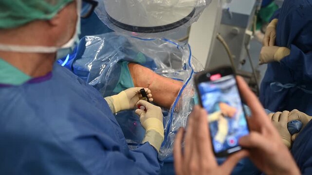 Surgeons performing knee arthroscopy while assistant records with smartphone