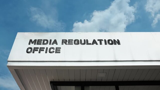 A media regulation office word sign displayed on an official building under a clear blue sky, symbolizing oversight, governance, policy, and compliance in communication