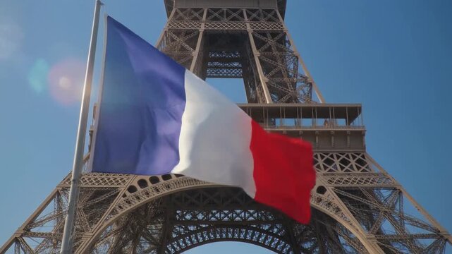 Ultra HD 8K video of the French tricolor flag waving elegantly in front of the Eiffel Tower under a clear blue sky, slow upward pan revealing the tower&rsquo;s iron structure, subtle lens flares, vibrant ye