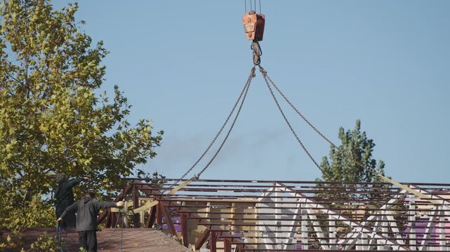 Crane lifting roof with slingers against blue sky