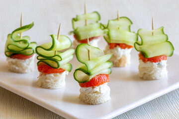 delicious canapes with cucumber, dill cream cheese and smoked salmon on square plate, appetizer for holiday party. Close up