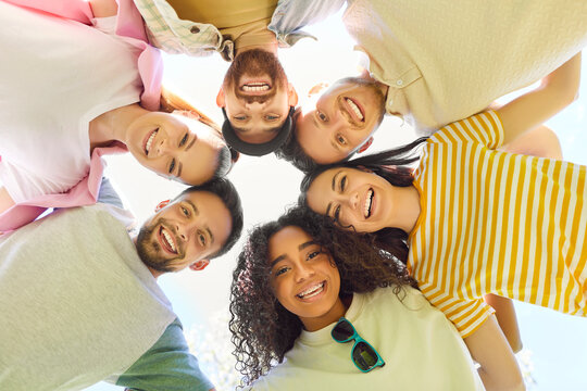 Fototapeta Friends together, group of young adults standing closely together in circle, looking downwards and smiling joyful, celebrating friendship and connection, sunny outdoor fun, pleasure or satisfaction