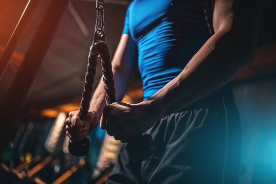 Closeup male bodybuilder performing triceps pushdown with rope in gym, Cropped shot man training arm muscles on cable machine during workout
