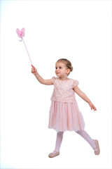 Rear view of a little girl in a pink tutu and ballet slippers, standing gracefully with a tiara on her head, holding pointe shoes.Little ballerina practicing dance moves. 