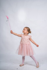 Rear view of a little girl in a pink tutu and ballet slippers, standing gracefully with a tiara on her head, holding pointe shoes.Little ballerina practicing dance moves. 