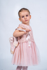 Rear view of a little girl in a pink tutu and ballet slippers, standing gracefully with a tiara on her head, holding pointe shoes.Little ballerina practicing dance moves. 