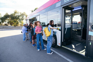 Girl checking the time on her watch while queuing for a city bus and diverse multi ethnic group of commuters lined up at a sunny city bus stop, boarding an electric public transport bus for daily trav