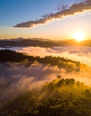 Naklejka premium Aerial view of a mountain range at dawn. The sun rises over the hills, casting a golden glow through the clouds