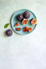 Purple ripe figs and slices with leaves on a plate top view on a stone background