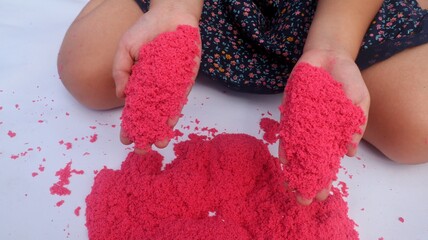 Child's Hands Playing Bright Pink Kinetic Sand close up view.