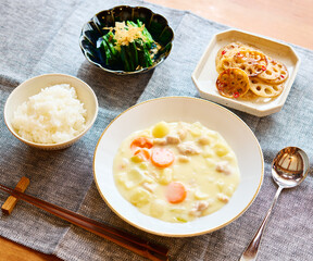 Japanese home-cooked meal with creamy stew, rice, spinach, and lotus root side dish on table