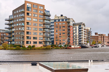Modern apartment buildings along Zaan River in Wormer, Netherlands, contrasting contemporary urban architecture with redeveloped historic industrial warehouses, symbolizing adaptive reuse waterfront