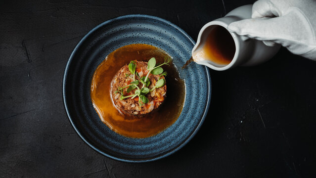 Close-up of a gourmet meal served on a blue plate with brown sauce poured from a jug. Elegant restaurant-style food presentation.
