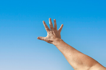 A hand is raised in the air with fingers spread against a blue sky background with space for text.