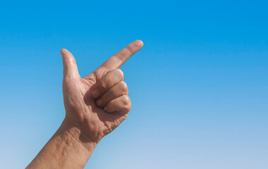 A hand is raised in the air with a sign made from fingers against a blue sky background with free space for text.