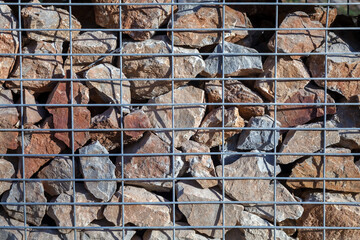 A stone wall is enclosed by a metal fence. A gabion fence is made of metal rods and installed on top of the stones.
