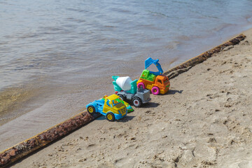 Three toy trucks are sitting on the beach next to a log
