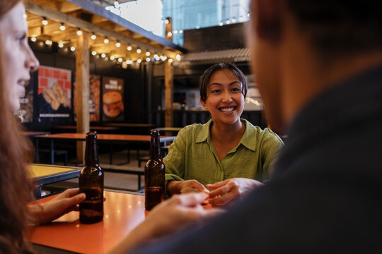 Friends talking and smiling at brewery bar with drinks in evening
