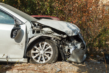 A white car lies in a pile of mud and rocks after an accident. The front end is smashed.
