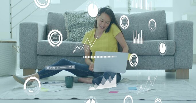 Typing woman in yellow top working on silver laptop in living room, with mug, data overlays - Powered by Adobe