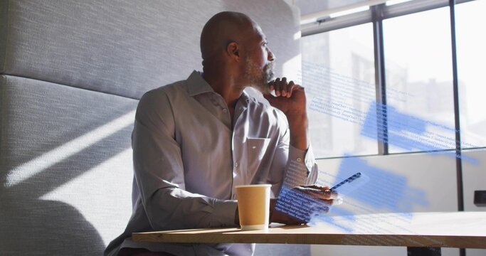 Businessman holding smartphone, gazing through window in office with tablet, coffee cup, copy space